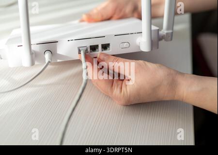 Close-up of a person plugging in an ethernet rj45 cable and power adapter into a wireless router with antennas. Concept of internet installation, tech Stock Photo