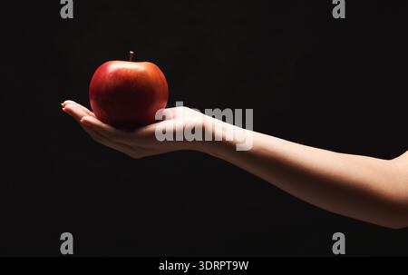 Hand Holding a Red Apple Against a Dark Background in a Simple Collage Design Stock Photo