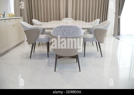 White and tan dining table with six chairs around it. The chairs are all different colors and patterns, and they are arranged in a circle around the t Stock Photo