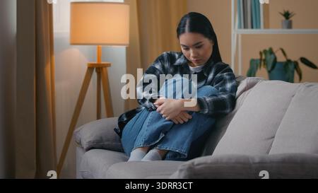 Sad worried Asian Korean woman sitting on sofa at home feeling anxiety depression psychological problem female mental health stress Japanese girl Stock Photo