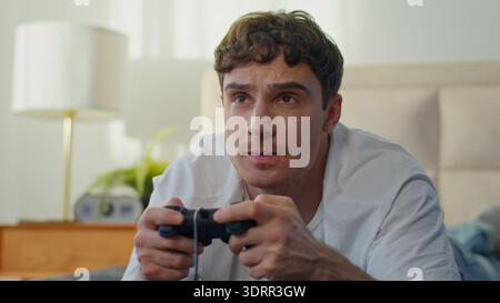 Upset Caucasian man lying bed playing losing video game joystick frustrated male guy loss failure defeat annoyed unhappy gamer struggling console Stock Photo