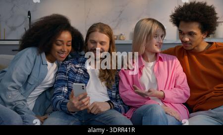 Multiracial friends men women ordering food delivery mobile phone at home couch together African American Caucasian girls guys discussing using Stock Photo