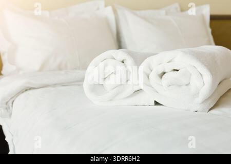 Collection of Rolled Towels on a Bed Set in a Cozy Room at a Hotel or Home in the Morning Light Stock Photo