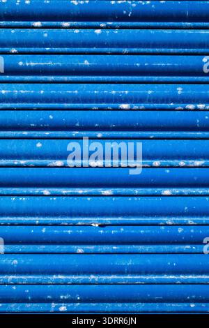 Close-up abstract texture of a weathered blue industrial metal shutter with horizontal ridges and peeling paint, ideal for background or design use Stock Photo