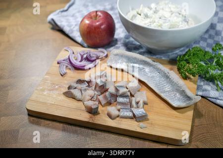 Chopped soused herring fillets on a cutting board, onions, apple, and herbs to make a fresh herring salad, ingredients for a traditional fish dish, co Stock Photo