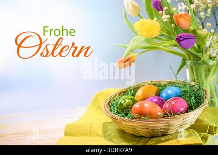 Basket with colorful painted Easter eggs and a spring bouquet with tulips, German text Frohe Ostern, meaning Happy Easter, light blue background, copy Stock Photo