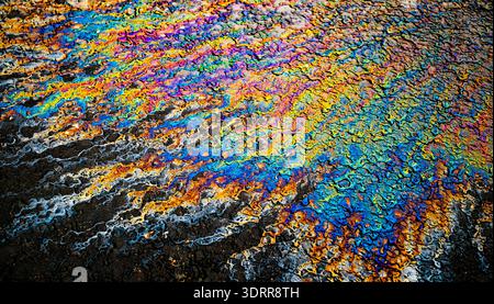 a photograph of an oil or petrol stain on a wet asphalt or pavement surface, a phenomenon called iridescence. interference of light waves reflecting o Stock Photo