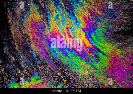 a photograph of an oil or petrol stain on a wet asphalt or pavement surface, a phenomenon called iridescence. interference of light waves reflecting o Stock Photo