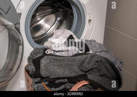 laundry basket with clothes in front of open washing machine Stock Photo