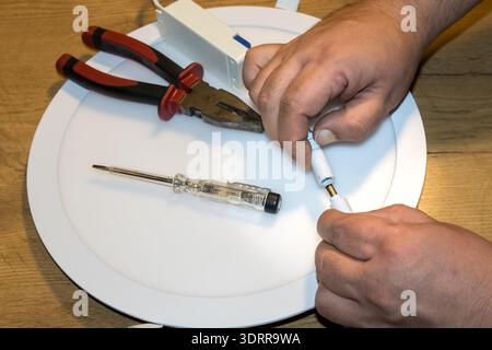 hands connecting electrical wires on led lamp with tools on work surface Stock Photo
