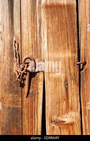 Rusty Vintage Metal Latch and Chain on Weathered Wooden Barn Door in Close Up Stock Photo