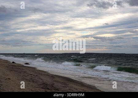 Rough ocean waves rolling onto sandy beach under layered stormy clouds creating a dynamic and atmospheric coastal landscape. Stock Photo