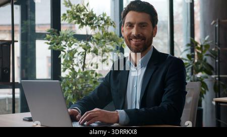 Caucasian businessman typing laptop office smiling looking at camera portrait professional male entrepreneur HR manager CEO leader employee working Stock Photo