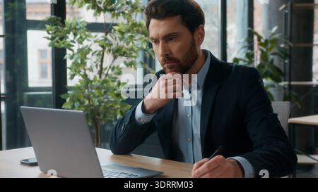 Thoughtful puzzled Caucasian office businessman typing laptop thinking analyzing information use computer professional male entrepreneur employee Stock Photo