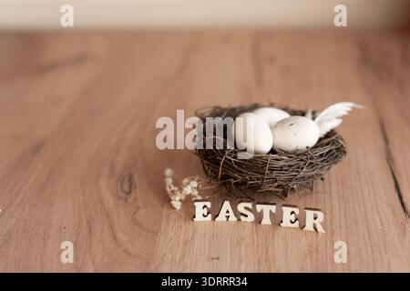 Easter nest with white eggs and wooden letters on rustic table. Minimal Easter still life bird nest with white eggs and feather on rustic wooden table Stock Photo