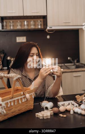 Woman crafting handmade decorations at home kitchen table. Woman crafting handmade decorations at kitchen table with basket of supplies, warm cozy Stock Photo