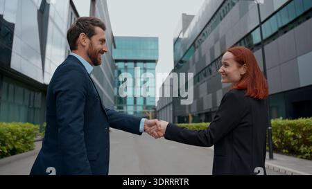 Back view two Caucasian business people greeting meet city partners handshaking woman man formal meeting colleagues talking discuss walking outdoors Stock Photo