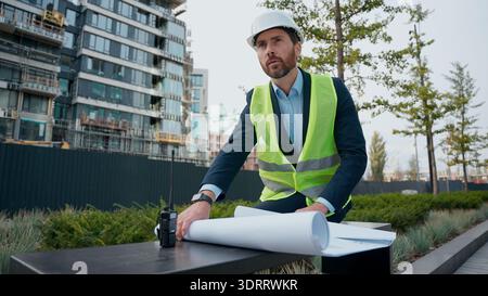 Pensive male architect thoughtful looking around check blueprint building plan think urban infrastructure manufacture thinking worker repairman man in Stock Photo