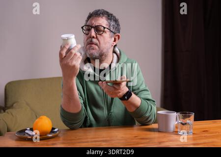 Mature man reading yogurt nutrition label while using smartphone at breakfast. Concept of healthy aging, mindful eating, ingredient awareness and digi Stock Photo