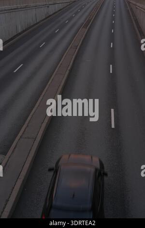 Car in motion blur moving through empty road with lane markings and concrete walls on both sides. City streets, empty freeway in evening or night time Stock Photo