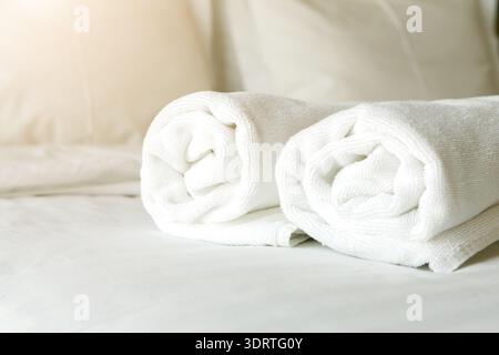Rolled White Towels Placed on a Clean Bed in a Bright Room With Soft Pillows and Sheets Stock Photo