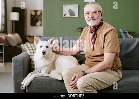 Portrait of Senior Caucasian Man Sitting with Dog on Sofa Indoors Stock Photo