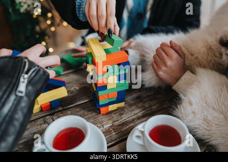 Girls build a colorful wooden block tower during a cozy, festive coffee moment Stock Photo