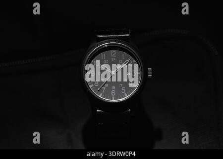 Close-up of a black analog wristwatch with a minimalist monochrome dial and visible date window, evoking precision, timekeeping, style and vintage mil Stock Photo