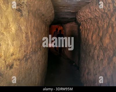 Two male silhouettes go into a dark cave, view from the back. Dark stone narrow corridor, background with copy space Stock Photo
