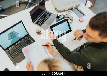 Teamwork in a modern office: two people collaborate using laptops, tablet, and documents at desk Stock Photo