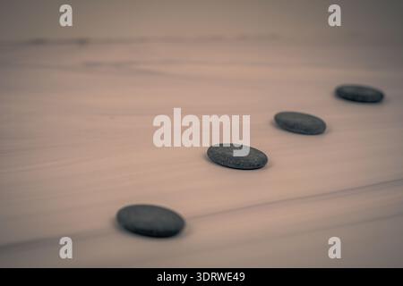 Minimal wellness background: smooth black spa stones arranged diagonally on marble surface, soft light and shallow depth of field, copy space. Stock Photo