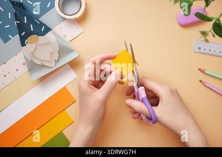 Hands cut duck out of yellow paper. Eraser, scissors, pencil on beige background. DIY handmade project for children. Stock Photo