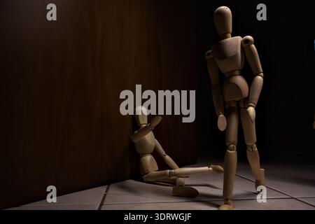 Wooden mannequin pretengind to sit on a street and to lean on a wall  raising its hand toward passing people in the act of begging  with other wooden Stock Photo
