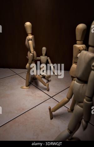 Wooden mannequin pretengind to sit on a street and to lean on a wall  raising its hand toward passing people in the act of begging  with other wooden Stock Photo