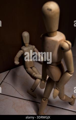 Wooden mannequin pretengind to sit on a street and to lean on a wall  raising its hand toward passing people in the act of begging  with other wooden Stock Photo