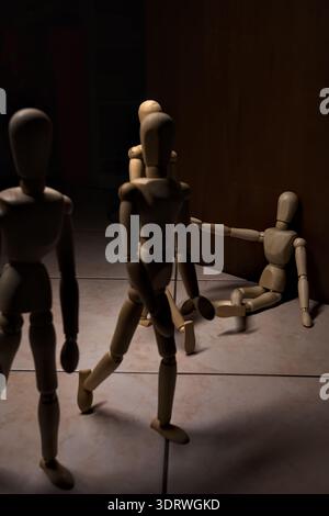 Wooden mannequin pretengind to sit on a street and to lean on a wall  raising its hand toward passing people in the act of begging  with other wooden Stock Photo