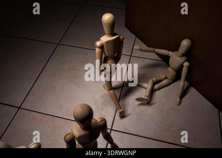 Wooden mannequin pretengind to sit on a street and to lean on a wall  raising its hand toward passing people in the act of begging  with other wooden Stock Photo