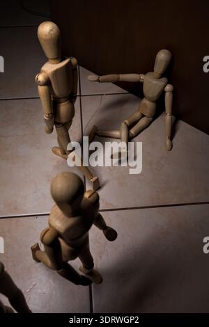Wooden mannequin pretengind to sit on a street and to lean on a wall  raising its hand toward passing people in the act of begging  with other wooden Stock Photo