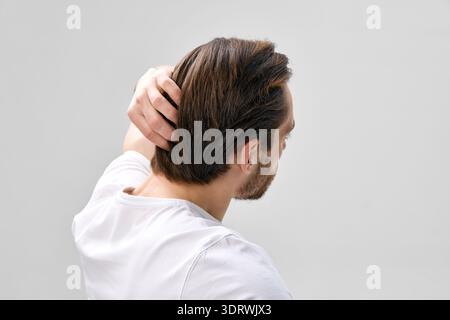 Rear three quarter side view of man in his thirties with short beard touching hair with one hand on light gray background Stock Photo