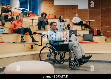 Inclusive classroom scene with diverse students and a man in a wheelchair engaging with devices during a group study Stock Photo