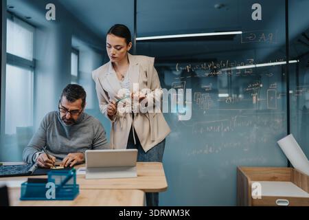 Collaborative office scene with a man writing and a woman guiding ideas at a glass wall for professional teamwork Stock Photo