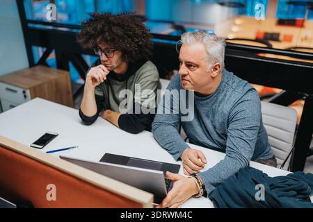 Two men collaborate at a bright modern office desk, focusing on a discussion and planning session Stock Photo