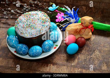 A photorealistic close-up of freshly baked Easter pastries: tall glazed cakes, golden buns, and painted eggs on a wooden table. A warm, soft backgroun Stock Photo