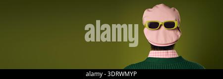 A stylish man poses in a green studio, wearing sunglasses over pink hat, banner Stock Photo