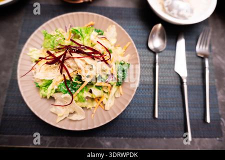 Fresh mixed salad with shredded beets and carrots served on ceramic plate with cutlery on dark textured table Stock Photo