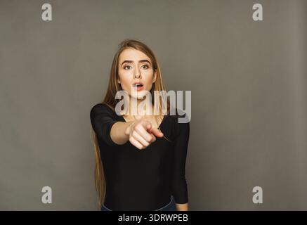 Surprised Woman in Studio Pointing at Something With Shock and Confusion Stock Photo