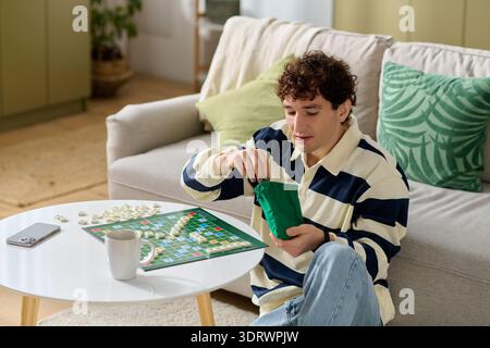 A young man relaxes in a cozy living room, unpacking game pieces for a fun night with friends. Stock Photo