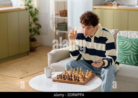 A handsome young man contemplates his next chess move while seated comfortably in his home. Stock Photo