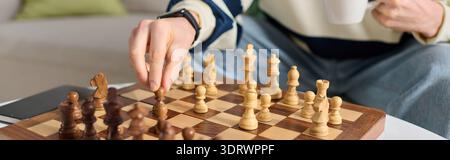 Handsome young man plays an engaging chess match while sipping his warm drink at home. Stock Photo