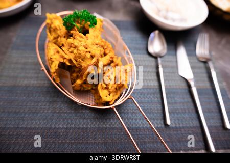 Indian Bhaji Fried Vegetable Fritters Served in Metal Strainer on Dark Table with Cutlery Stock Photo